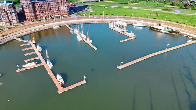Marina of Lelystad, the Netherlands with few boats and ships at the berths. Cityscape with lush greenery at backdrop. Aerial view.