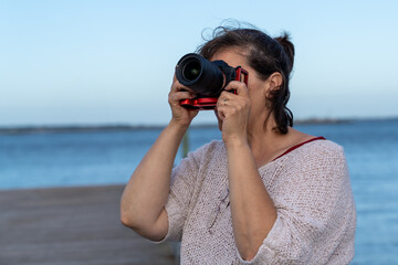 A woman is taking a picture of the ocean with a red camera. The water is calm and the sky is blue