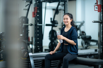 Young asian woman in activewear sitting in gym and drinking water after workout, healthy lifestyle, hydration, and post-exercise recovery concept