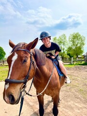 Smiling young woman riding a brown horse outdoors on a sunny day. Horseback riding, animal bonding, and equestrian lifestyle in natural countryside environment.