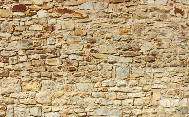 A close-up view of a textured stone wall featuring irregular patterns and warm, earthy tones, showcasing natural stone placement and historic craftsmanship.