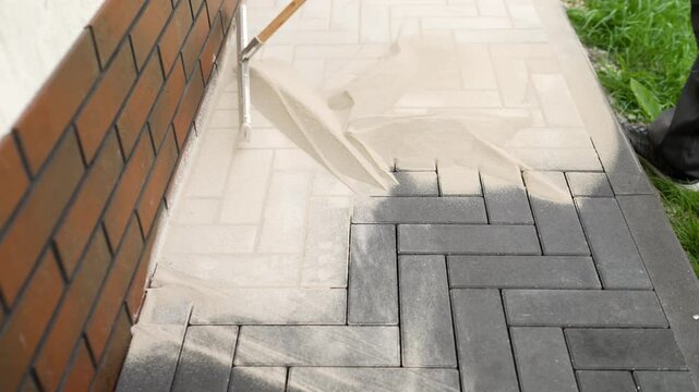 Construction worker uses a squeegee to spread sand over paving stones, creating a smooth and level surface