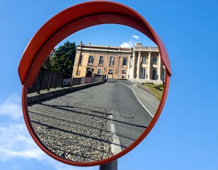 Convex mirror reflecting a road and classical buildings on a sunny day.