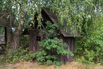 A small wooden cabin is surrounded by trees and bushes