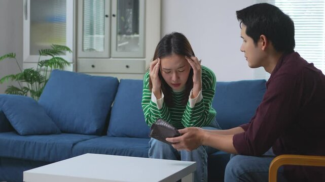 Financial stress weighing down young Asian couple, partner revealing empty wallet during intense conversation about monetary challenges at home