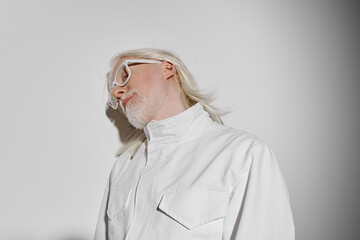 Portrait of a stylish older man with long white hair and glasses against a light grey background,...