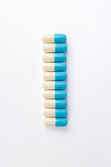 Blue and white medical capsules lined vertically Vertical row of blue and white pharmaceutical capsules on a clean white background, symbolizing medication and healthcare treatment. 