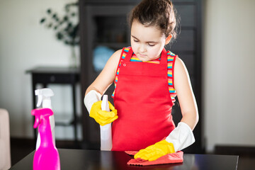 Cute little kid girl cleans table in living room at home. Child helping her mother.