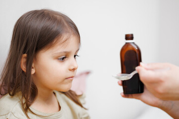 child is sick in bed. Mom gives cough syrup to her daughter. Concept disease, pharmaceutics.