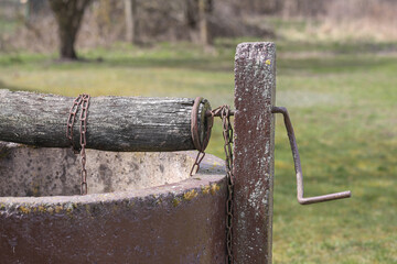 Old rural water well. Rusty crank wooden beam. Chain on winch. Village well. Historic tool. Country life background. Ancient water source. Traditional construction. Outdoor scene.