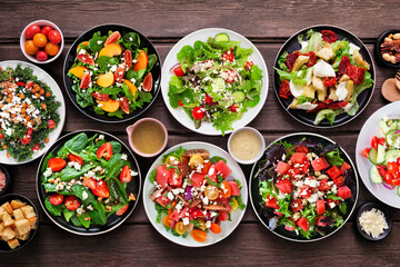 Assortment of delicious fresh salads. Top view table scene on a dark wood background. Summer food concept.