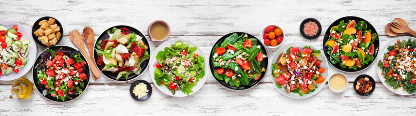 Assortment of delicious fresh salads. Top down view table scene on a white wood banner background. Summer food concept.