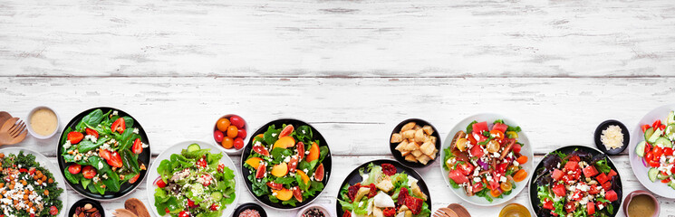 Assortment of delicious fresh salads. Top view bottom border on a white wood banner background. Summer food concept.