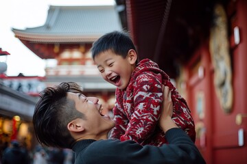 A cheerful father lifts his son in the air, both laughing joyfully in front of a temple's red facade.