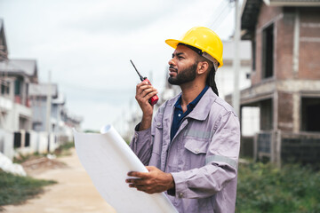Civil Engineer in Safety Helmet Using Radio at Construction Site with Blueprint