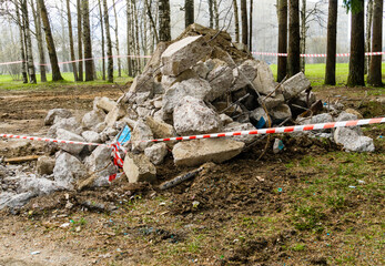 Concrete waste demolition pile marked red and white warning lines of barrier tape. City park.