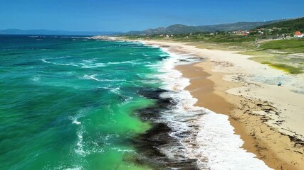 An aerial view showcases a stunning sandy beach, framed by turquoise waves and surrounded by lush green scenery