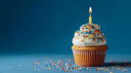 A single cupcake with white frosting and sprinkles and a lit candle on a blue background space for text