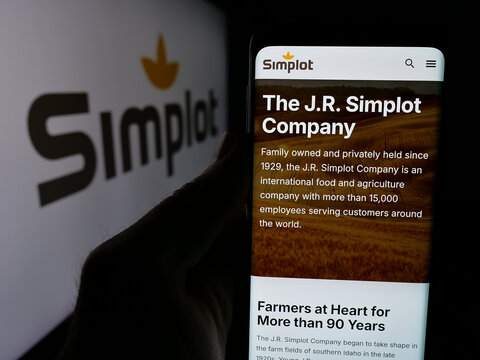 Stuttgart, Germany - 04-26-2025: Person holding cellphone with web page of US agribusiness J. R. Simplot Company on screen in front of logo. Focus on center of phone display.