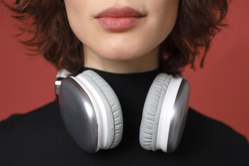 Close-up of a woman with wireless headphones around her neck. Focus on lips and modern audio gear. Stylish minimalism against red background