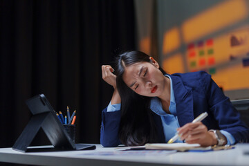 Young business woman feeling overwhelmed and fatigued from long hours at her office desk, battling...