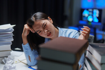 Overworked and tired businesswoman looking at pile of books and paperwork during night shift at...