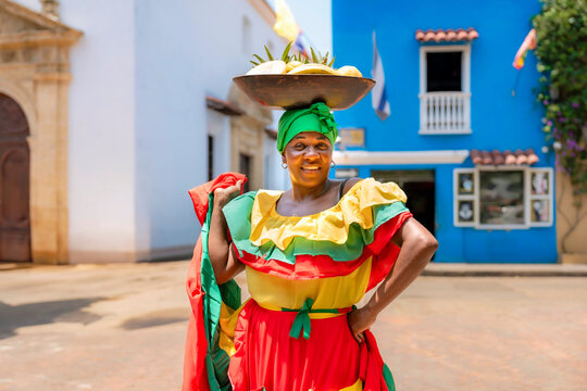 Afro-Latina Palenquera in colorful red, yellow and green dress holding skirt wide, with fruit bowl on her head in Cartagena, Colombia. Palenqueras are symbols of Afro-Colombian heritage.