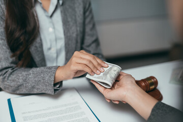 Lawyer handing wad of cash to client as bribe during legal proceedings in courtroom with gavel on...
