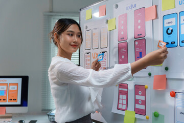 Young professional woman working on user experience and user interface of a mobile application, attaching sticky notes to a whiteboard