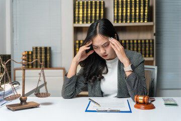 Young Asian lawyer experiencing a headache while tackling a challenging case in her office, surrounded by legal documents and pressure