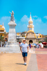 Latino man wearing sunglasses, gray shirt, and blue shorts standing confidently in Cartagena's main...