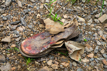 Old worn leather boots among stones on the river bank. Interesting texture close-up.