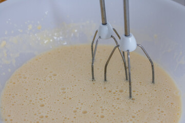 Bowl of batter is being mixed with a mixer. The batter is light and fluffy. The whisk is silver and...