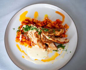 Sliced grilled chicken breast served with diced cooked carrots and creamy sauce on a white plate, top view.