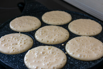 Uncooked pancakes with bubbles on a hot griddle, close-up of batter cooking in round molds during...