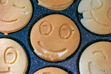 Cute smiley face pancakes cooking on a black speckled griddle, fun and cheerful breakfast in progress.