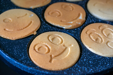 Cute smiley face pancakes cooking on a black speckled griddle, fun and cheerful breakfast in...