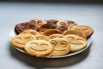 Plate of emoji face pancakes in various shades, playful breakfast concept on a light wooden surface.