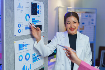 Confident businesswoman explaining charts and graphs during a team meeting, highlighting data analysis and strategic planning in a modern office setting
