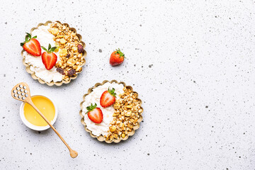 Tasty homemade dessert with cottage cheese, granola and juicy aromatic strawberries on white marble background top view. Healthy breakfast concept.