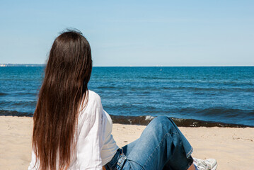 Young caucasian woman with long brunette hair relaxing on a sandy beach wearing casual jeans and a...