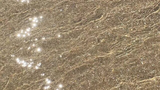 Close-up image of a sandy beach with gentle waves forming delicate patterns on the surface. Captures the serene natural textures and details of the shoreline.