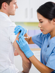 A healthcare provider in blue scrubs carefully gives a vaccination to a man seated in a clinical environment. The moment captures attention to health and safety protocols.