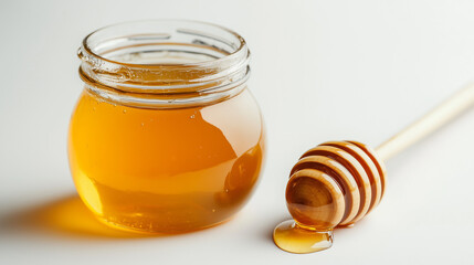 Golden honey cascading from wooden dipper beside filled glass jar, white backdrop