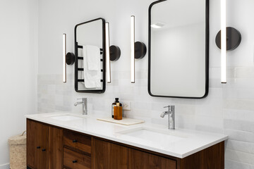 A bathroom detail with a dark wood vanity cabinet, white marble countertop, black sconce lights...