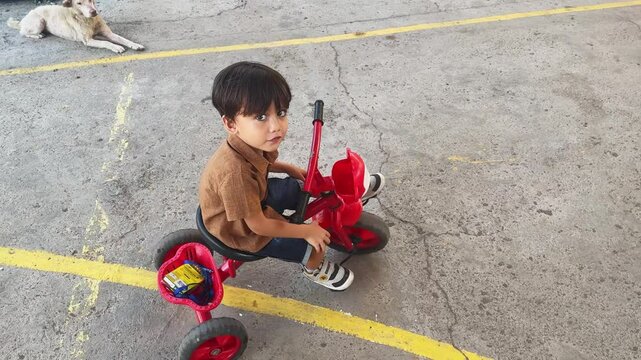 Doubting boy looks up riding tricycle along city street