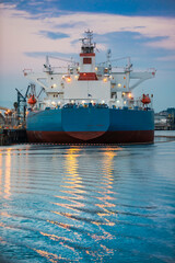 Container ship at dusk with lights reflected in the water