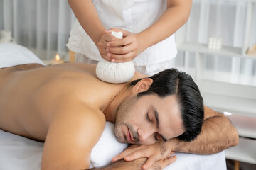 Hot herbal ball spa massage body treatment, masseur gently compresses herb bag on man body....