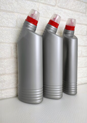 Three plastic bottles for cleaning products, intended for household chemicals or sanitary products against the background of a light brick wall. 