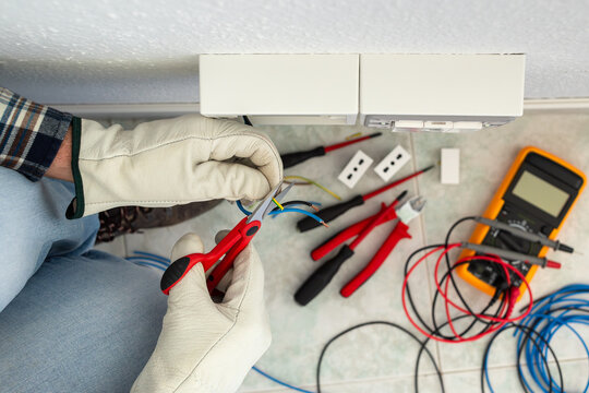 Electrician worker at work with scissors prepares the electrical cables of an electrical system. Working safely with protective gloves. Construction industry.